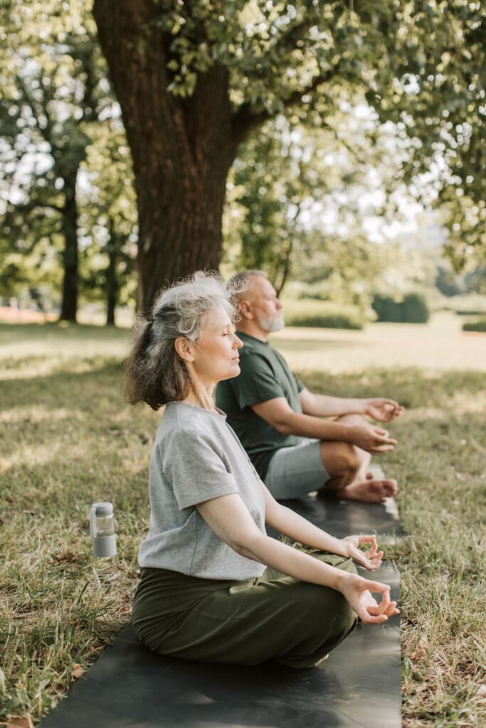 Elderly couple practicing meditation together on yoga mats in a sunny park