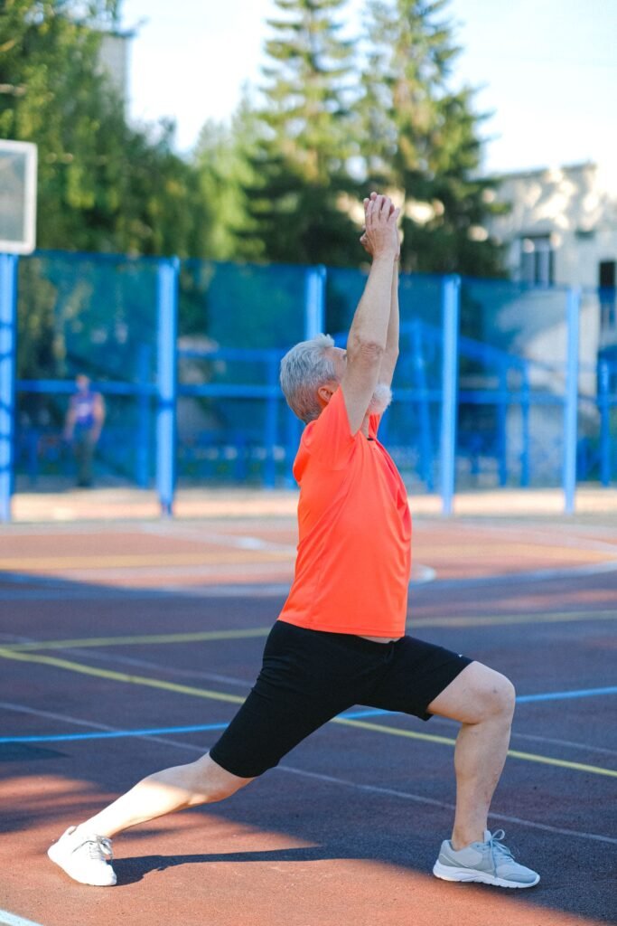 Elderly man in yoga warrior pose outdoors, focusing on fitness and wellness.