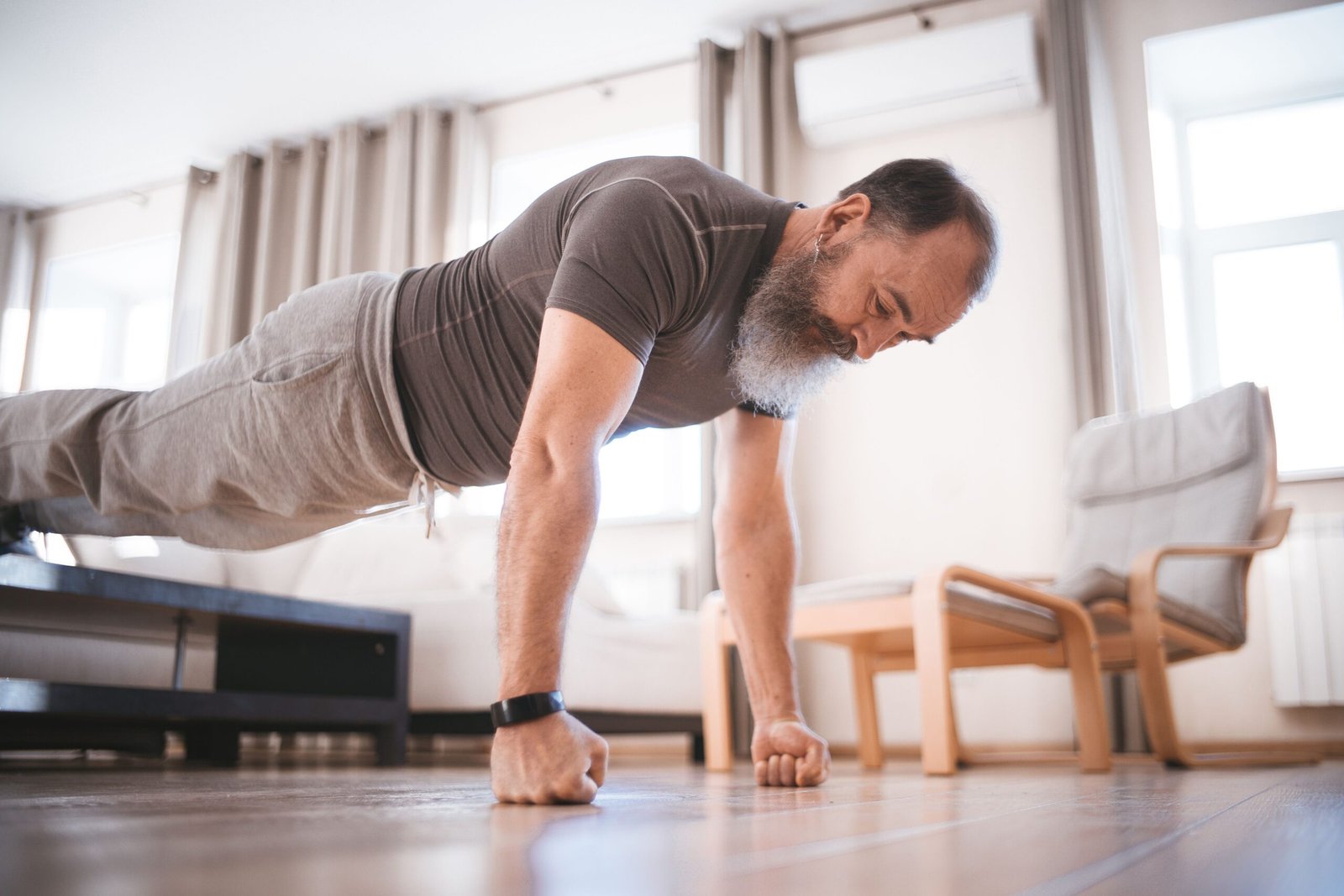 Elderly man performing a push-up at home in a bright living room