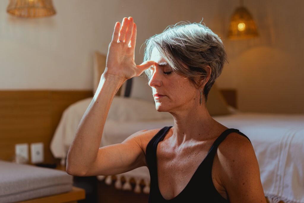 Older woman sitting in meditation indoors, eyes closed, practicing mindfulness