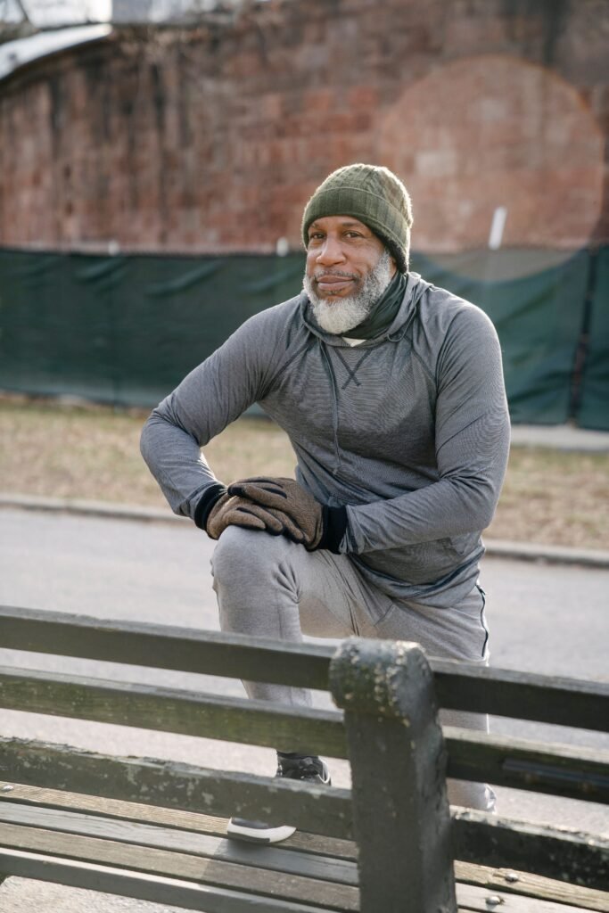 Elderly Black man stretching his legs outdoors in a city park, warming up before exercise