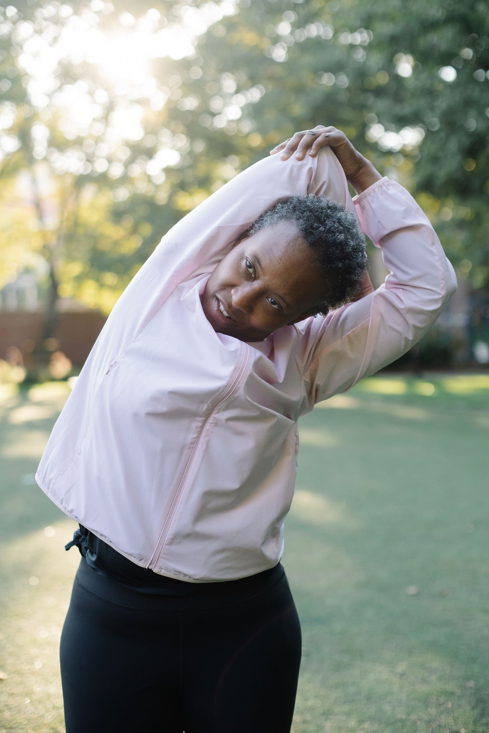 Elderly Black woman exercising with stretches in a sunny park setting, promoting healthy lifestyle.