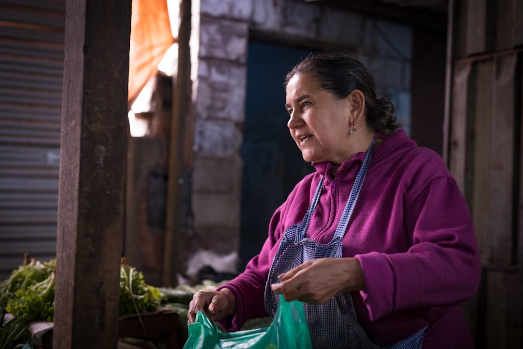 An older woman selling fresh vegetables at an outdoor market stall
