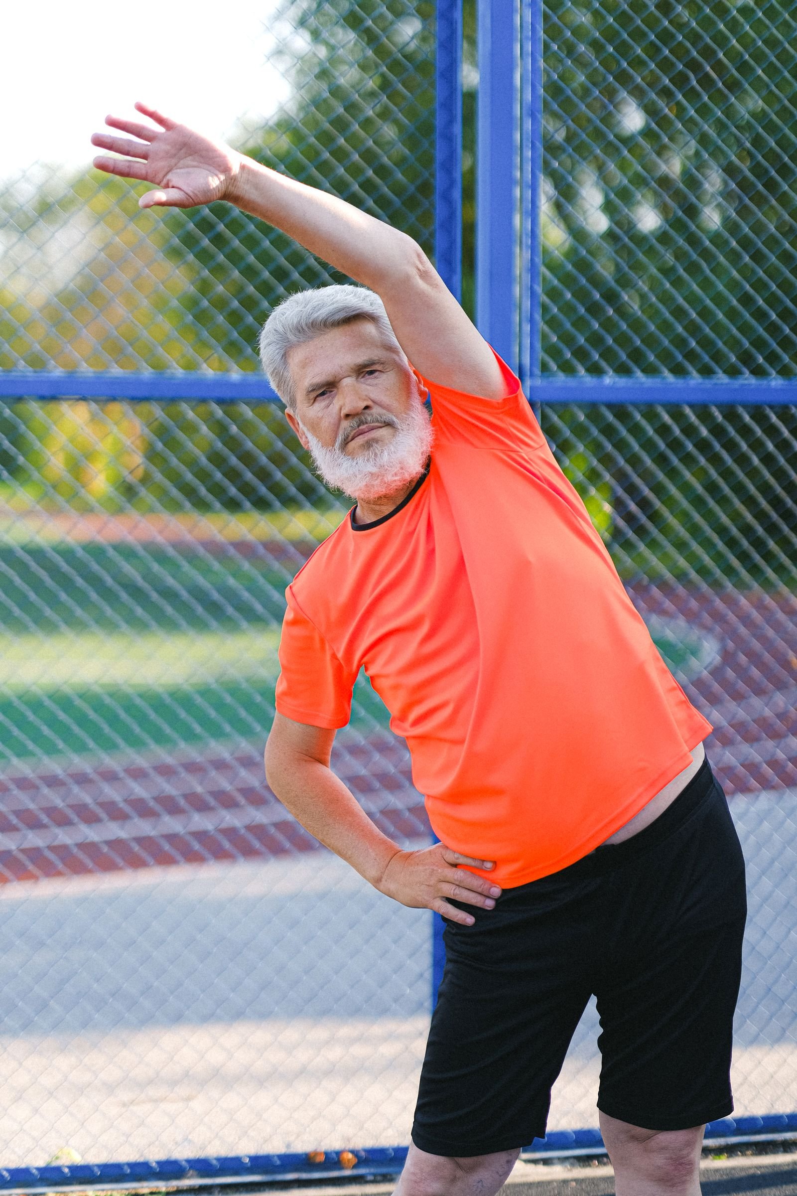 Senior man in sportswear stretching outdoors on a sports field.
