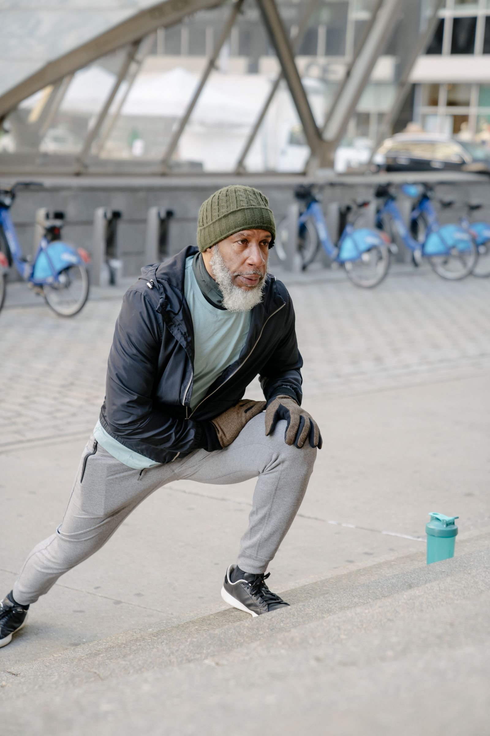 Elderly Black man stretching his legs on outdoor stairs while warming up before training.