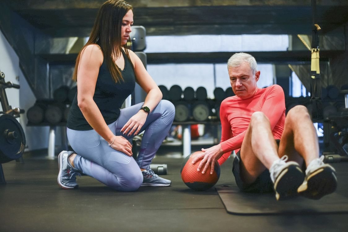Senior man doing a guided shoulder exercise with a personal trainer in the gym