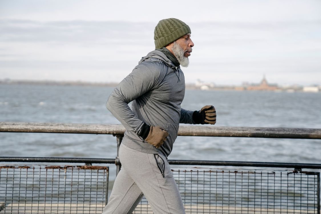 Senior Black man running along a waterfront path during morning exercise