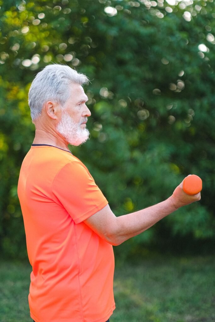 Senior man in bright sportswear doing dumbbell curls outdoors in a park