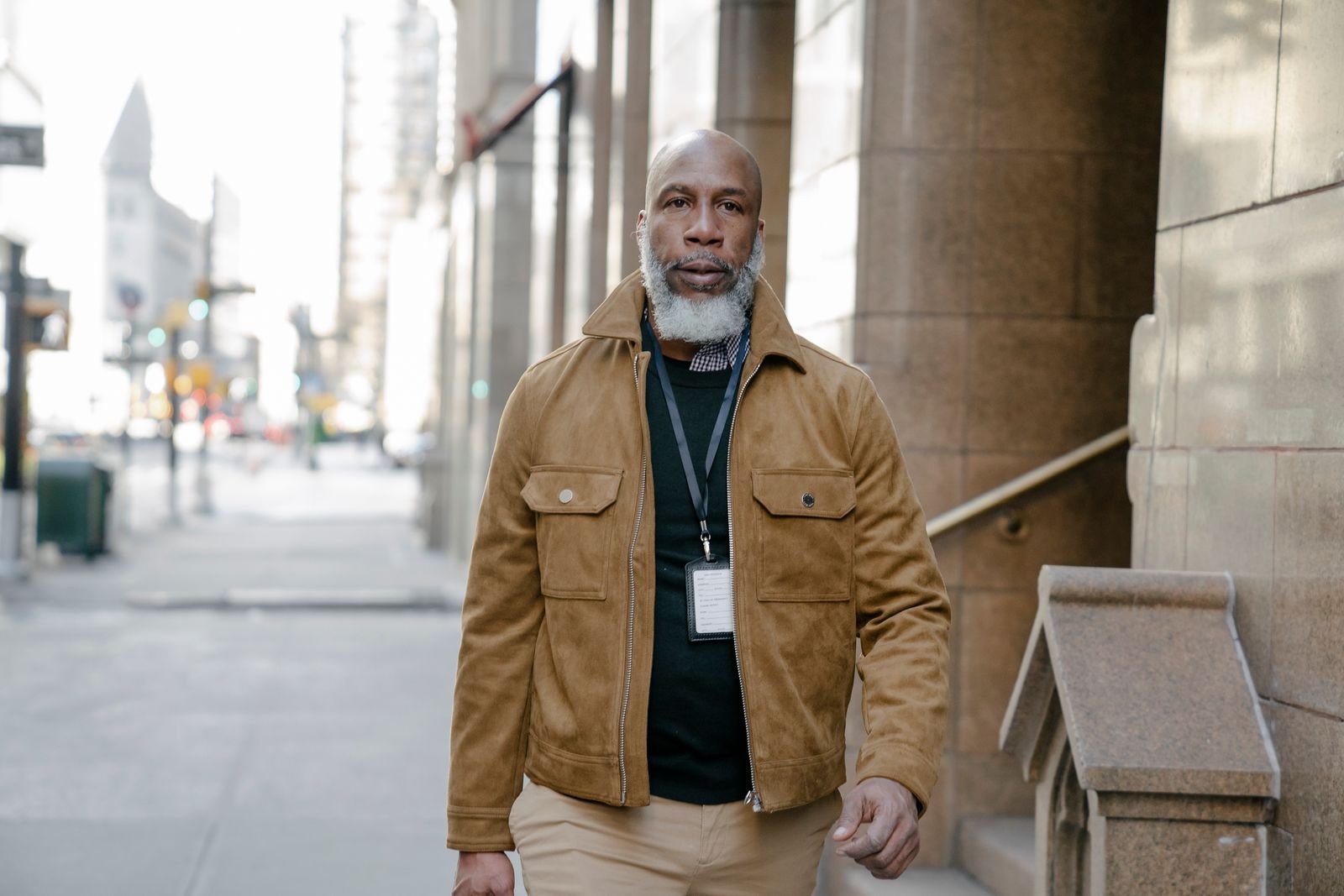 Older Black man with a gray beard walking confidently along a city sidewalk