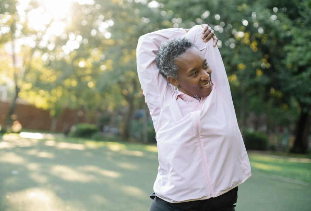 Older African American woman doing a standing stretch outdoors in a sunny park