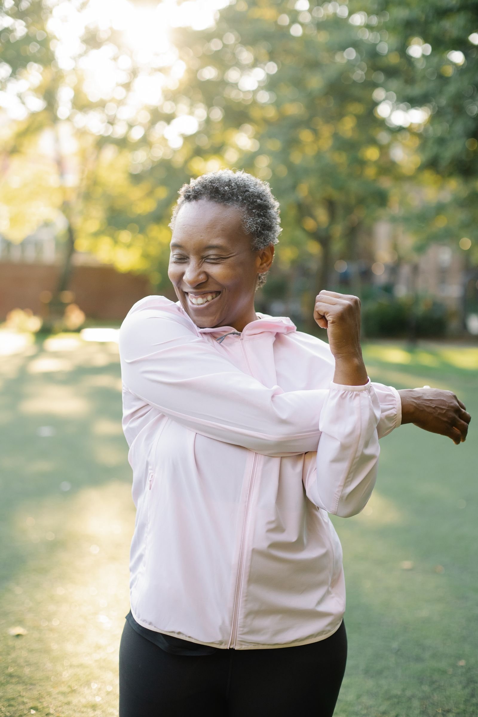 Smiling Black woman in her sixties stretching her arms in a sunny park before a walk