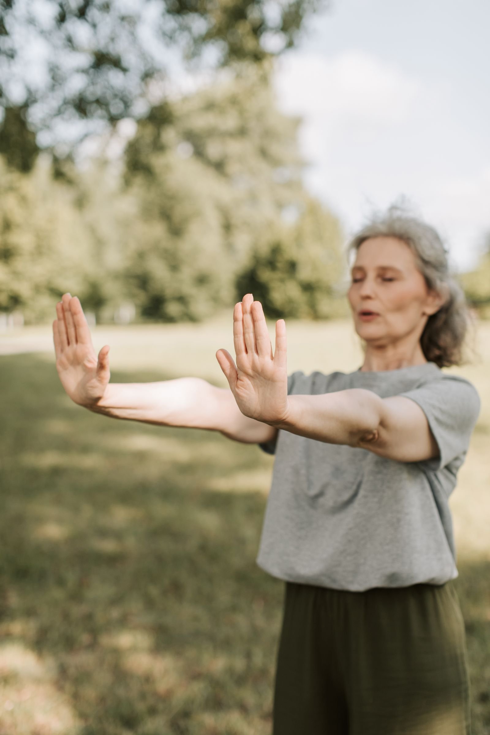 Senior woman practicing gentle tai chi movements outdoors in a park