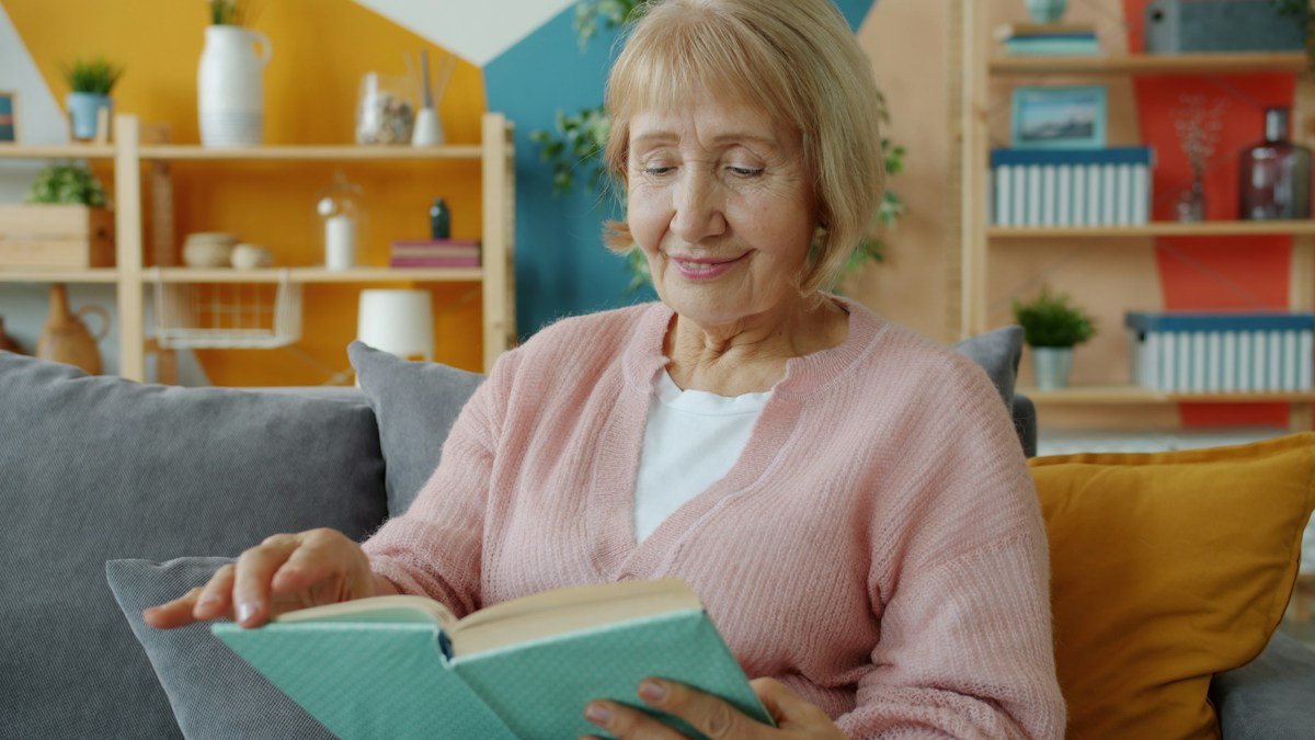 Smiling senior woman reading a book at home, staying mentally engaged