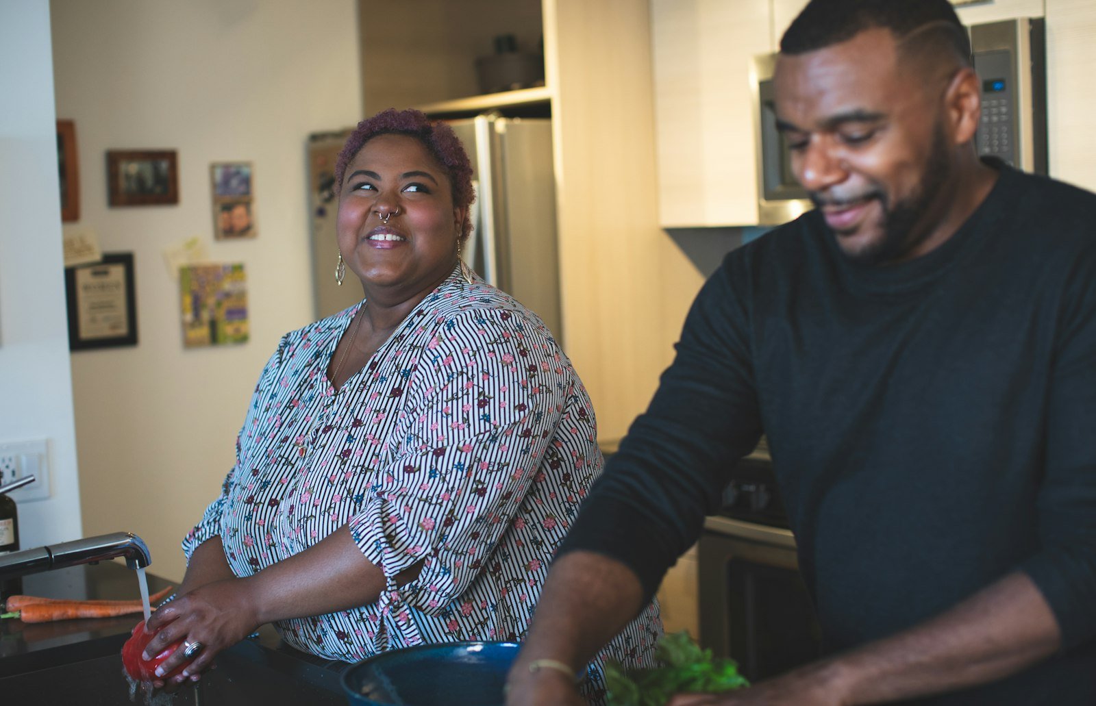 A Black couple washing fresh vegetables together at the kitchen sink