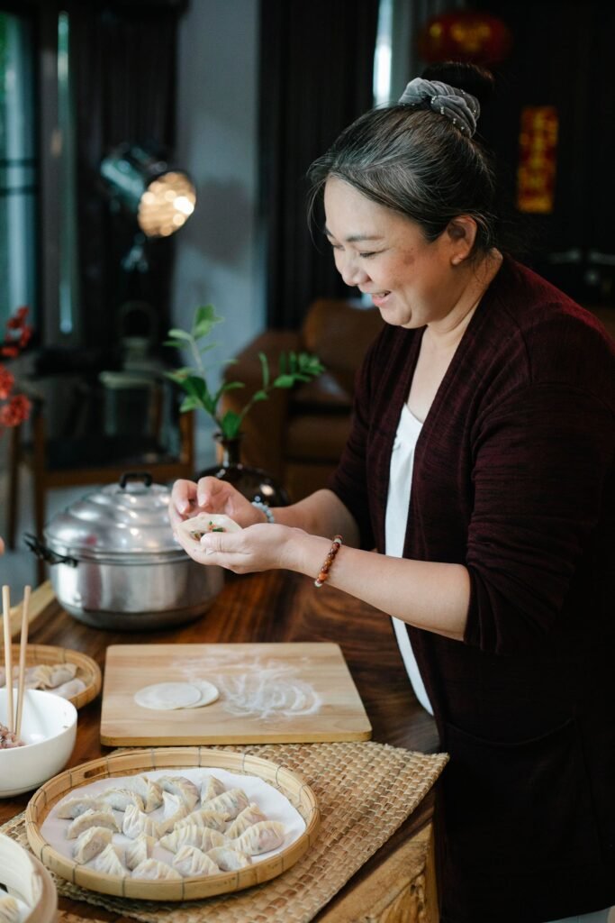 Smiling Asian woman in her sixties preparing homemade dumplings at her kitchen table