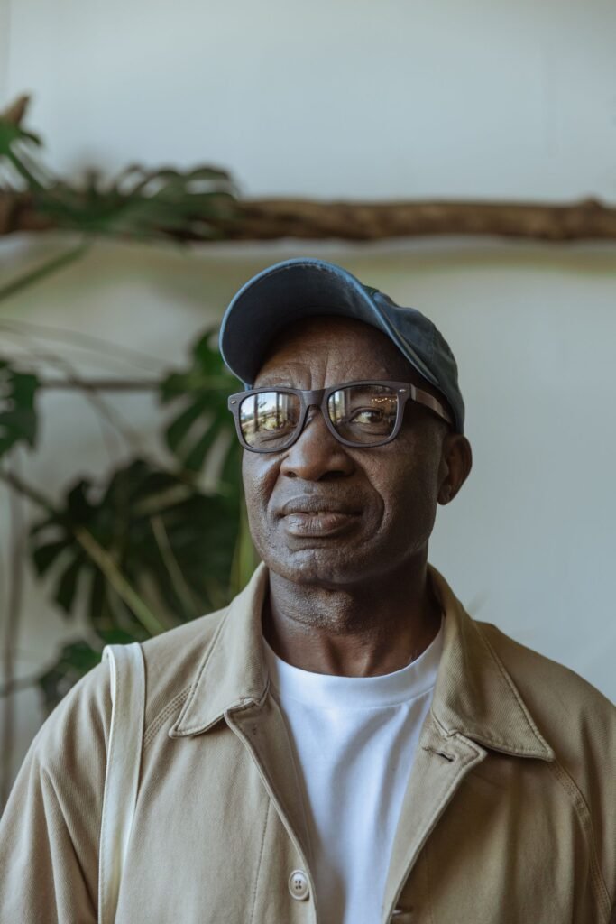 Older Black man in eyeglasses and a baseball cap smiling at home