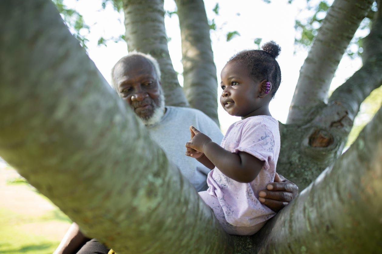 Grandfather playing outdoors with children by a tree