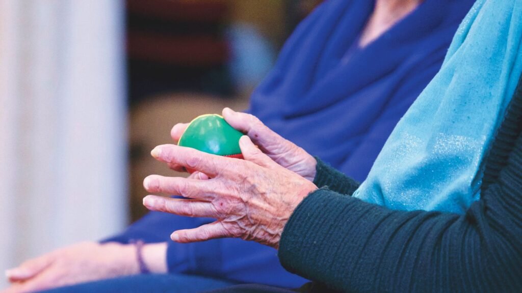 Close-up of an older adult’s hands squeezing a green therapy ball