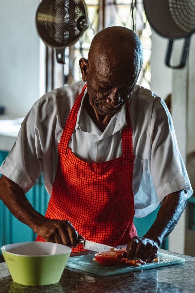 Older Black man in a red apron cooking a meal at home in his kitchen