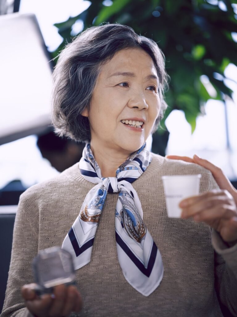 Smiling older Asian woman in a scarf holding a cup, relaxed and engaged