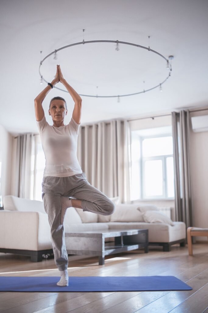 Older woman holding a tree pose on one leg in her bright living room