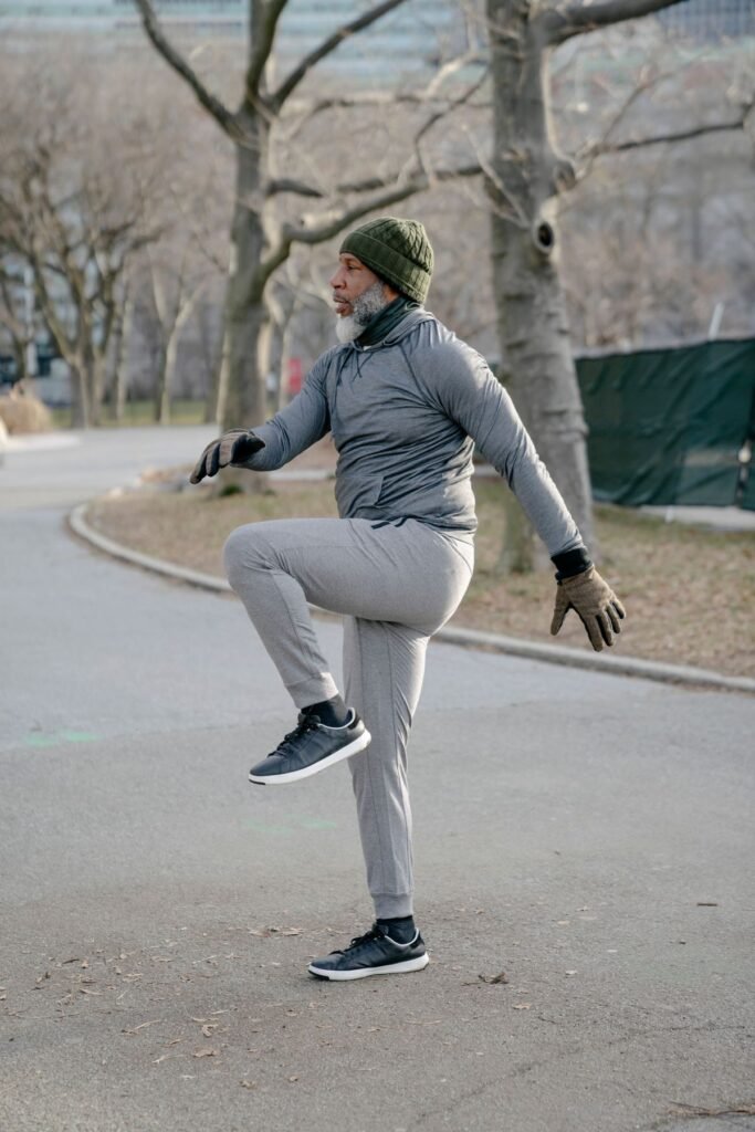 Older man in sportswear doing a standing knee raise on a park path