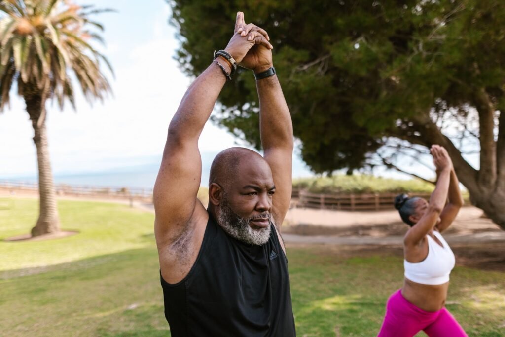 Senior Black man raising his arms overhead during an outdoor yoga session in a park