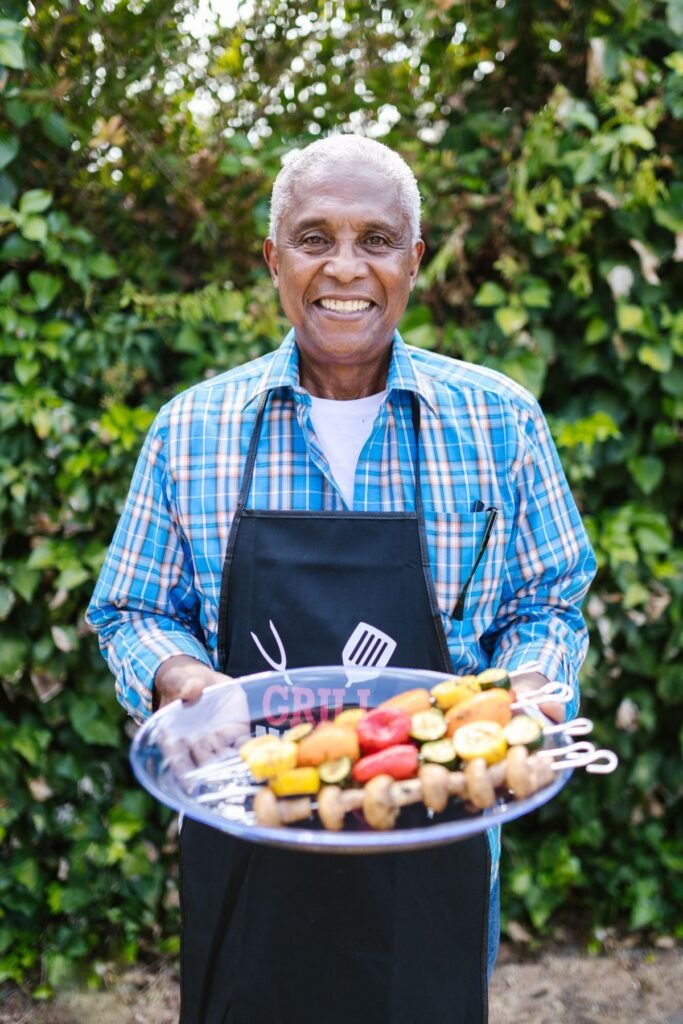 Smiling older man in an apron holding a platter of fresh fruit and vegetables